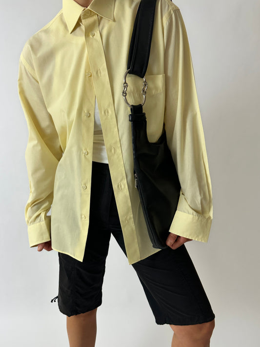 Person wearing a light yellow shirt and black shorts with a black bag over one shoulder on a white background