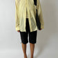 Person wearing a light yellow shirt, black shorts, and black shoes on a white background