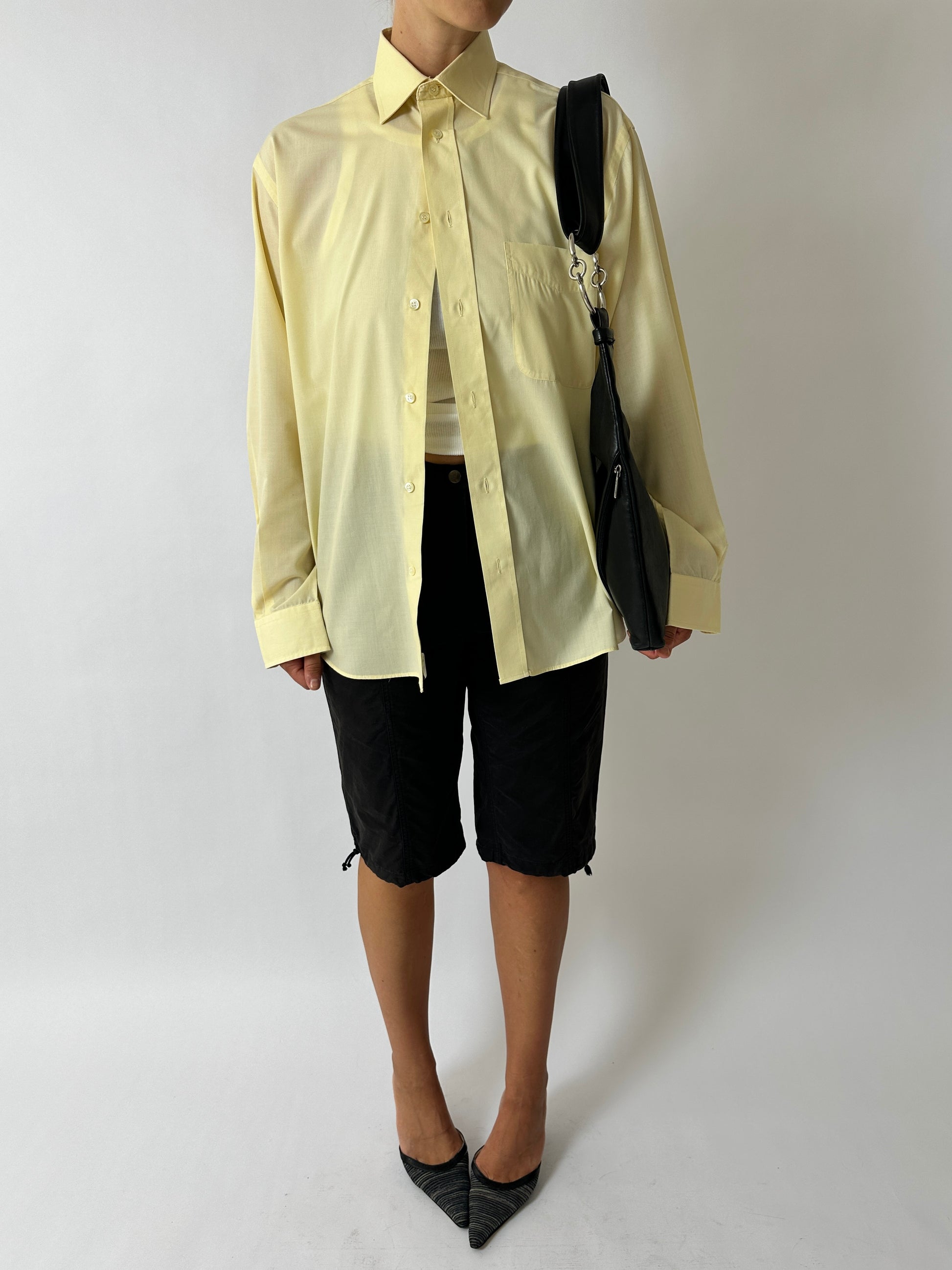 Person wearing a light yellow shirt, black shorts, and black shoes on a white background