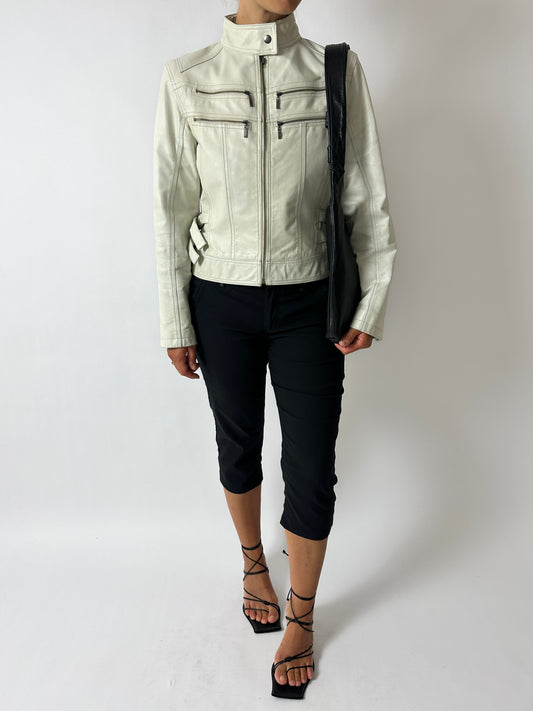 Person wearing a light-colored leather jacket and black pants on a white background