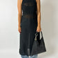 Person wearing a black sleeveless dress holding a black handbag on a plain background
