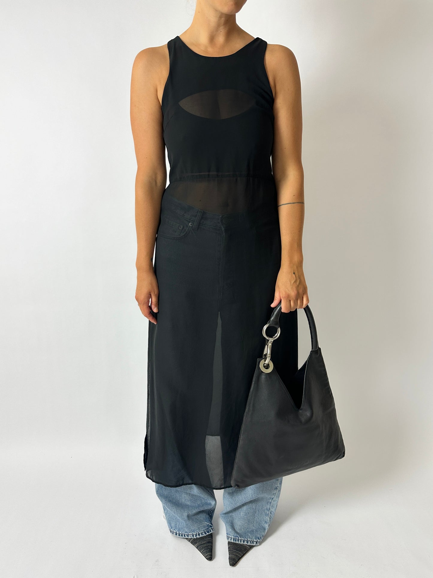 Person wearing a black sleeveless dress holding a black handbag on a plain background
