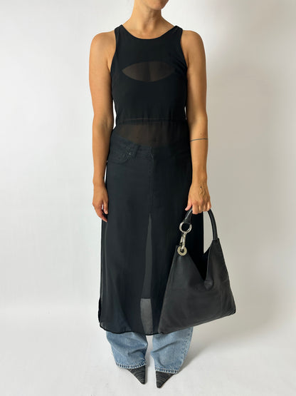 Person wearing a black sleeveless dress holding a black handbag on a plain background