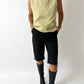 Person wearing a light yellow sleeveless jacket, black pants, and black boots on a white background