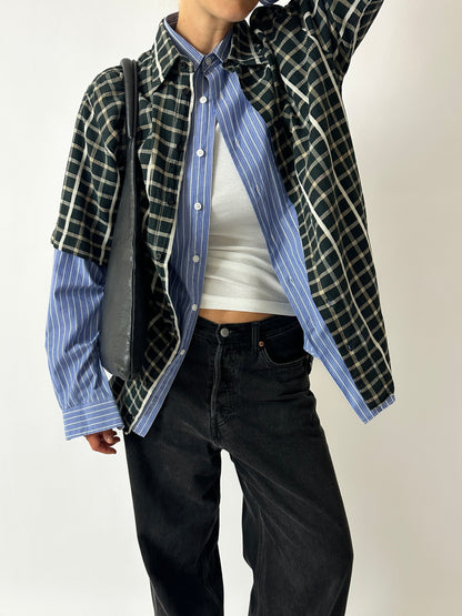 Person wearing a layered outfit with a plaid shirt, striped shirt, and black pants on a plain background