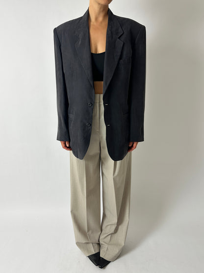 Person wearing a black blazer and beige pants on a plain background
