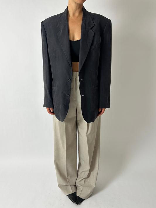 Person wearing a black blazer and beige pants on a plain background