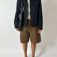 Person wearing a black jacket, white shirt, brown shorts, and black shoes on a white background
