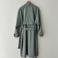 Green trench coat on a hanger against a white wall