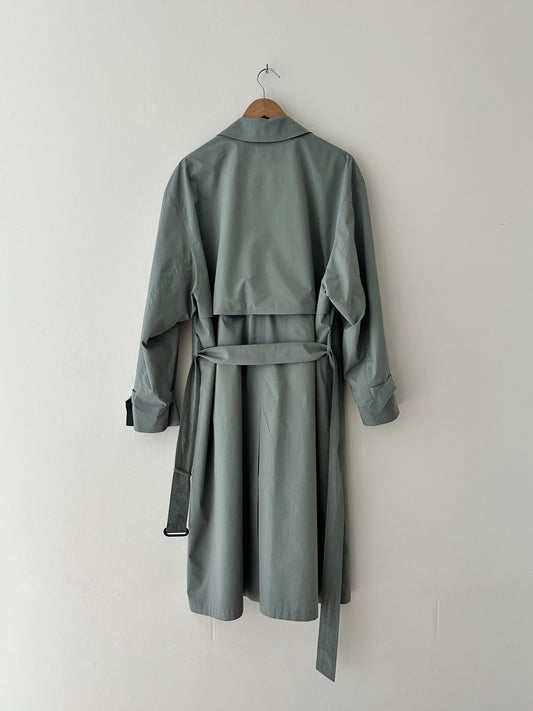 Green trench coat on a hanger against a white wall