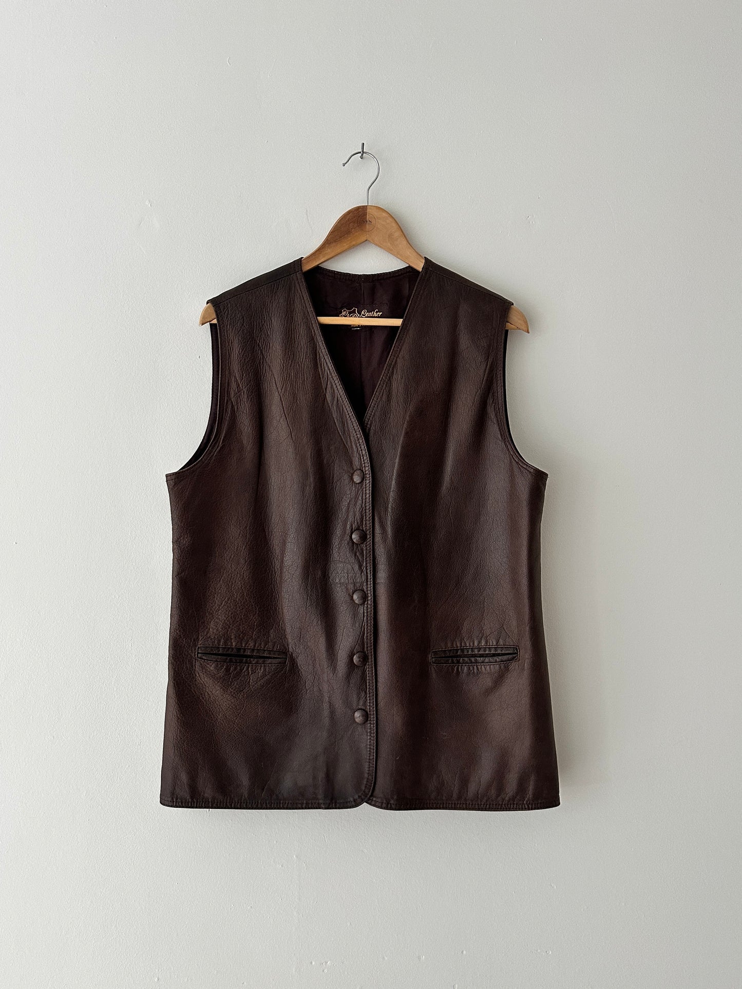 Brown leather vest on a wooden hanger against a white background