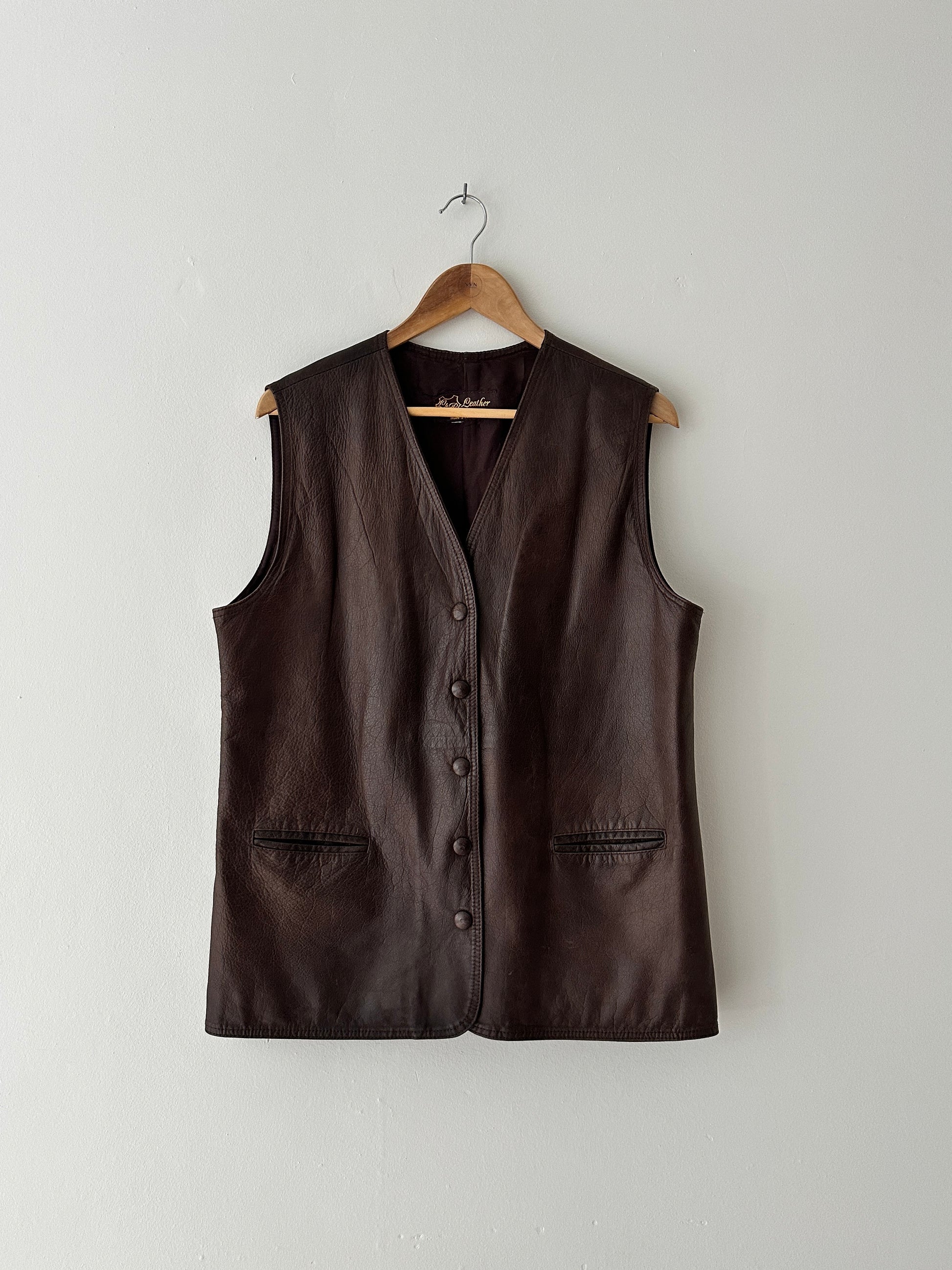 Brown leather vest on a wooden hanger against a white background